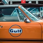 Side view of a vintage orange car with Gulf branding, showcasing retro automotive style.